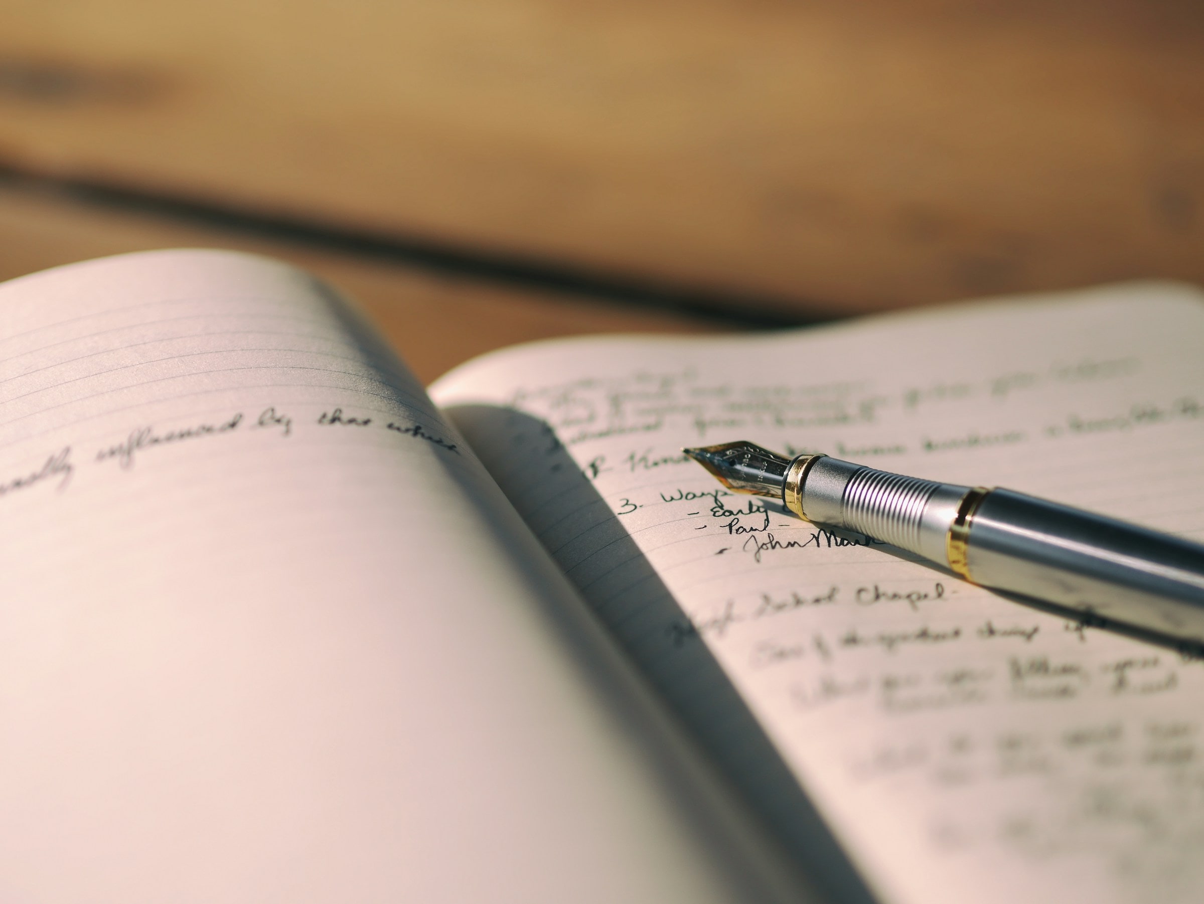 An open notebook with handwritten notes and a pen on a wooden desk
