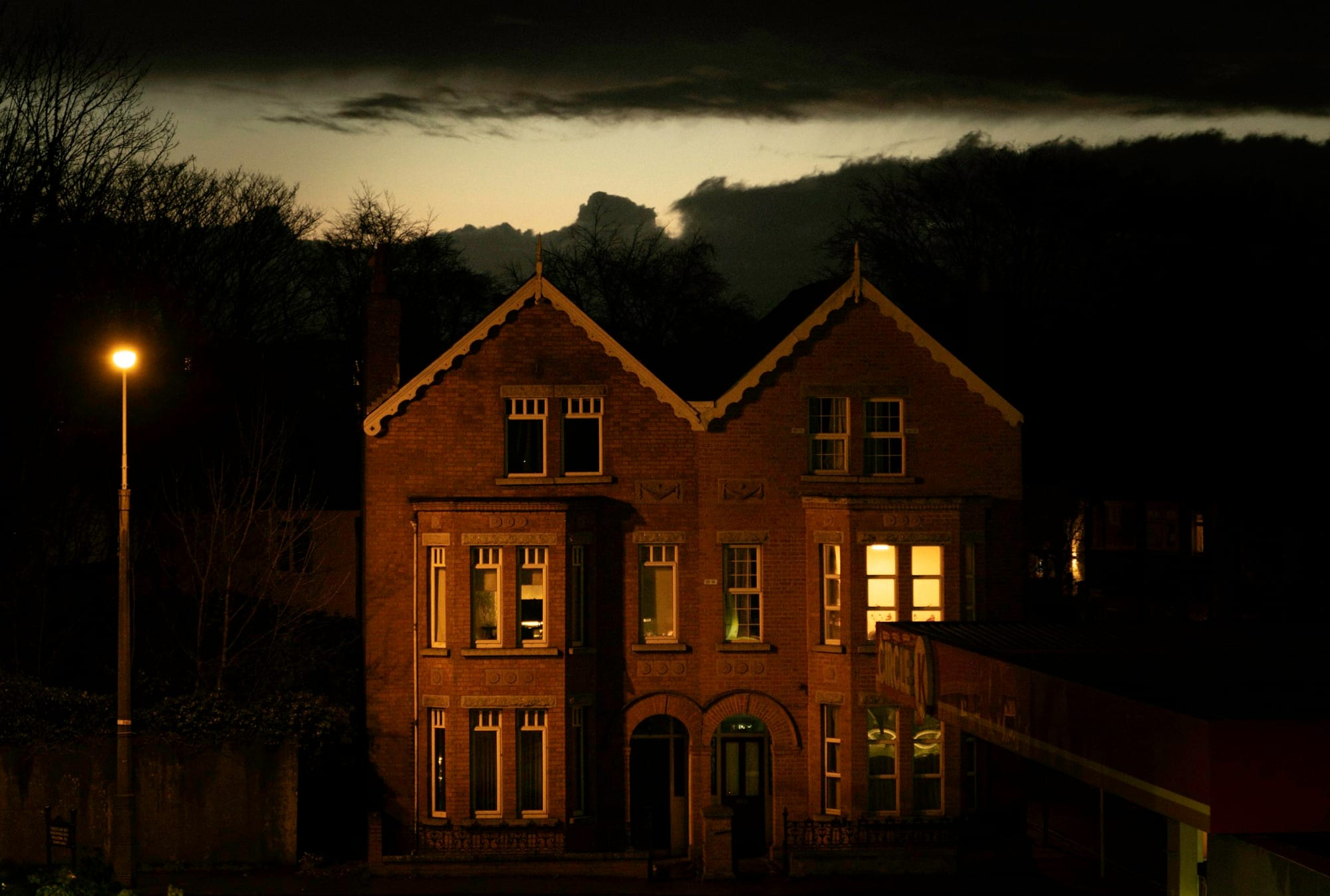 A residential property at night, its left side in deep shadow where the door an agent would knock on sits unlit.
